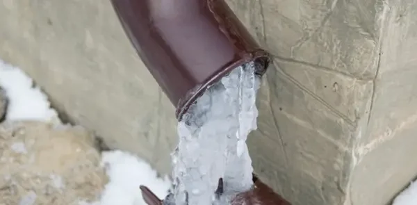Exposed plumbing pipe frozen solid with ice expansion, indicating risk of burst or water supply blockage
